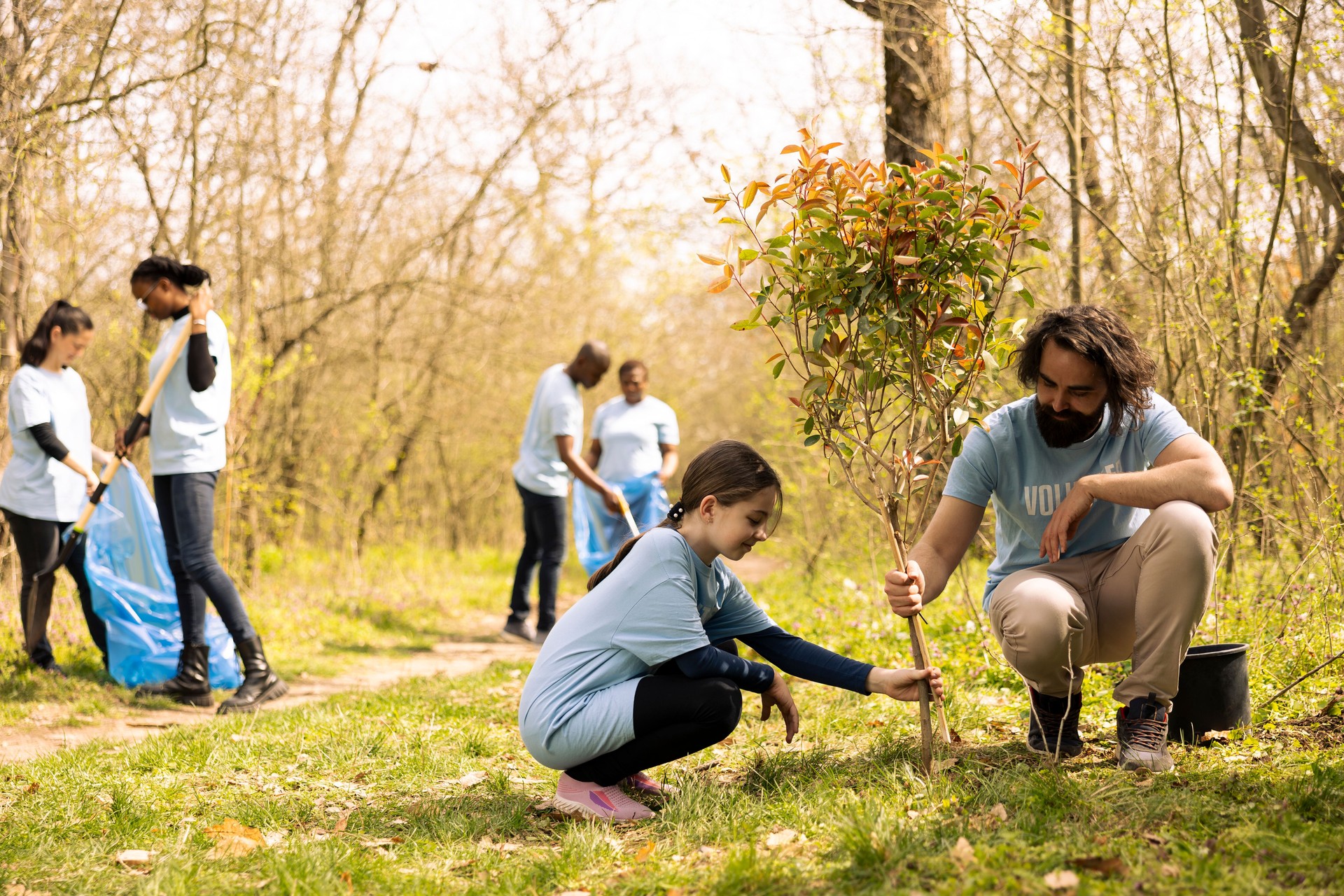 Volunteer and small girl collaborate on planting a tree together