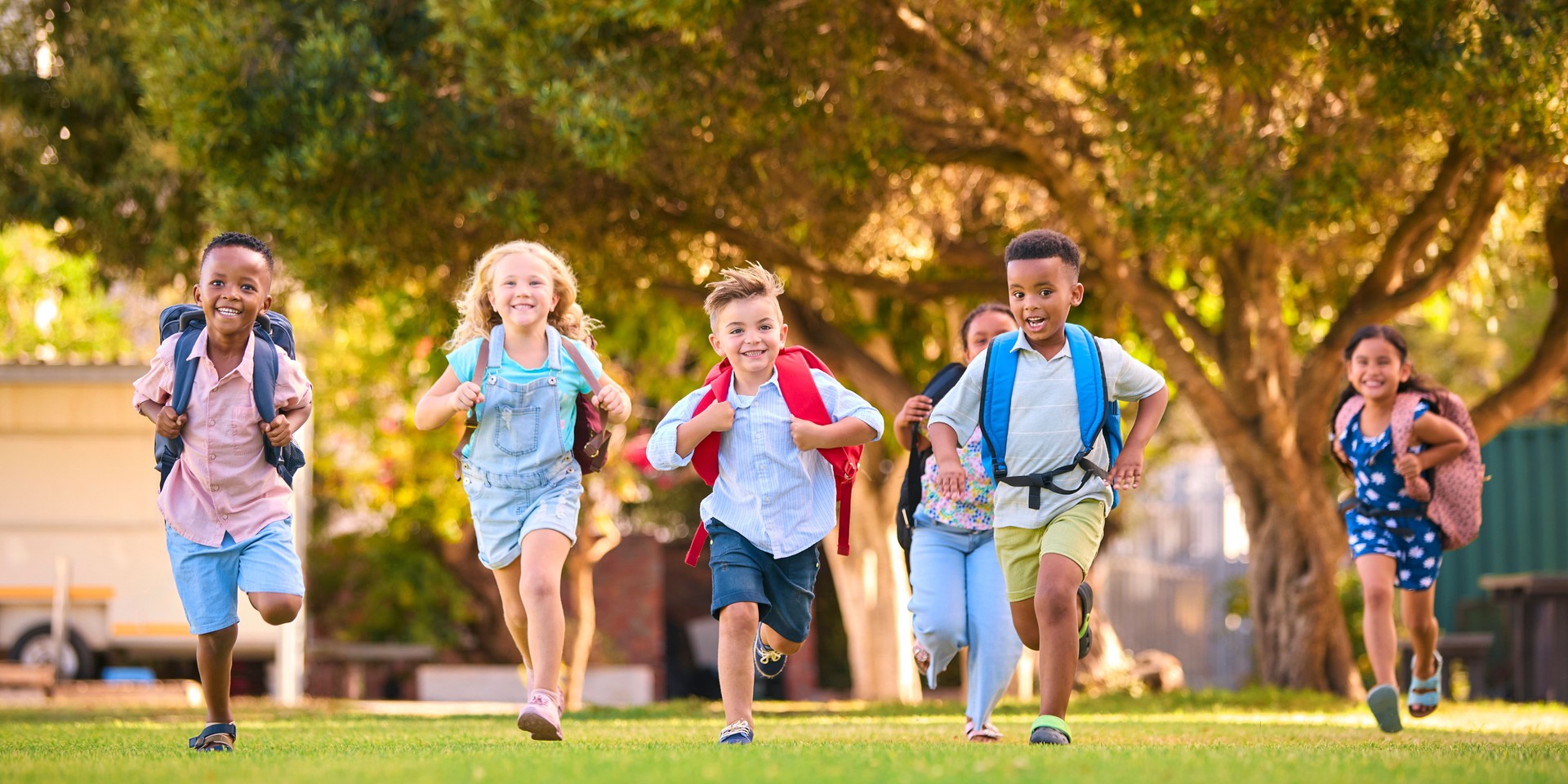 Multi-Cultural Primary Or Elementary School Students With Backpacks Running Outdoors At End Of Day